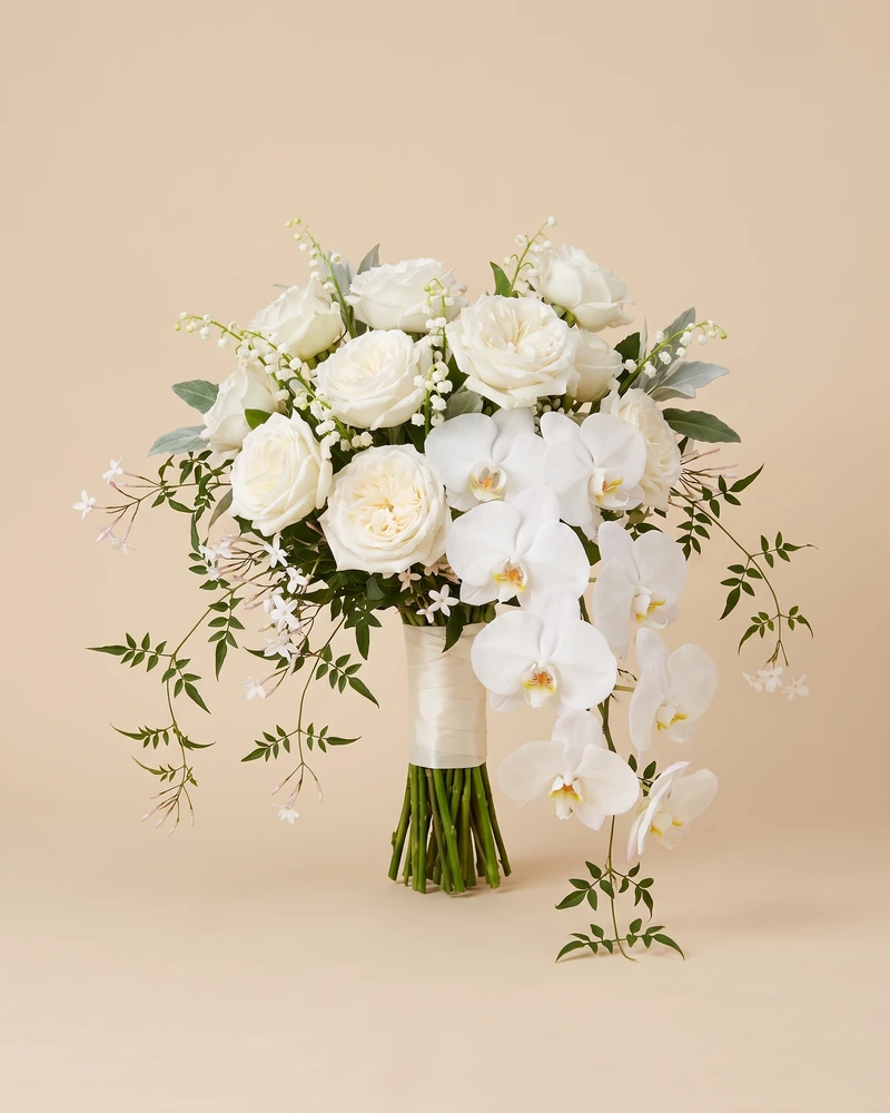 Bouquet de mariée en cascade&nbsp;: roses blanches, orchidées phalaenopsis retombantes, muguet et jasmin, manche en ruban satin ivoire.